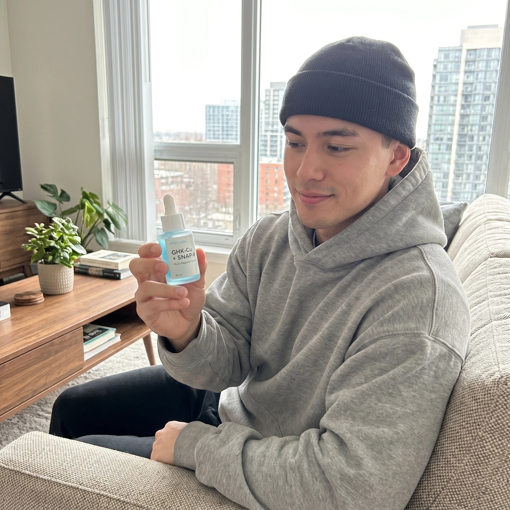 Customer holding KRM Labs GHK-Cu and SNAP-8 Multi-Peptide Serum on couch