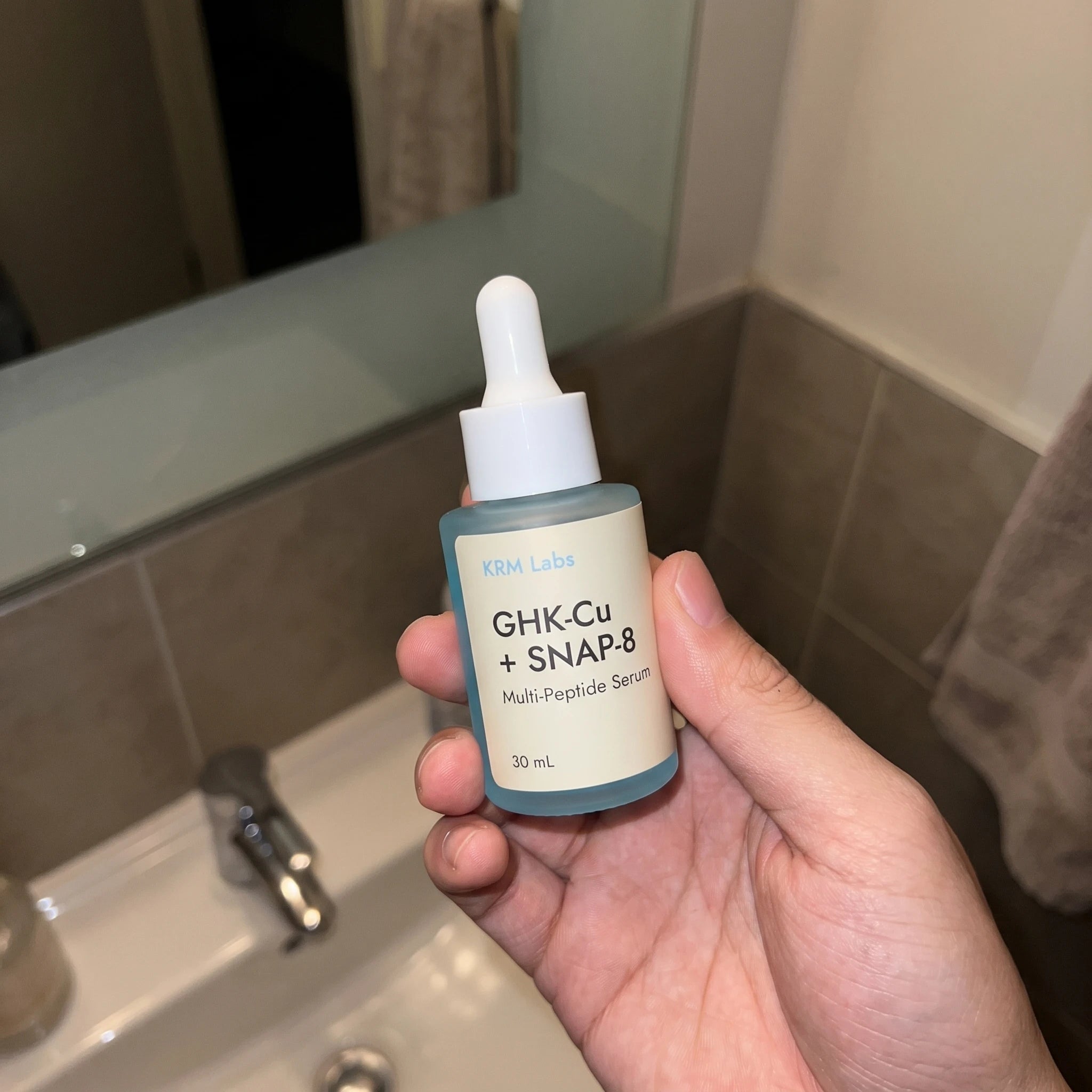 Customer holding KRM Labs serum in robe at bathroom counter